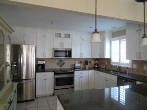 A modern kitchen with stainless steel appliances, white cabinetry, and a granite countertop. - Amazing Sunsets, Sound Front View, Private Dock (Ocean Isle Beach)