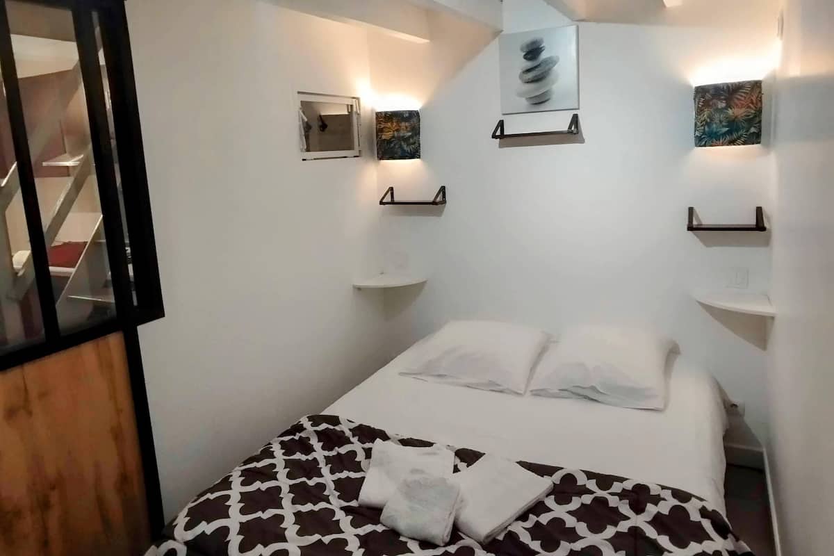 Une chambre à coucher avec un lit, une petite fenêtre et des étagères fixées au mur.