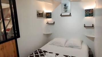 Une chambre à coucher avec un lit, une petite fenêtre et des étagères fixées au mur.