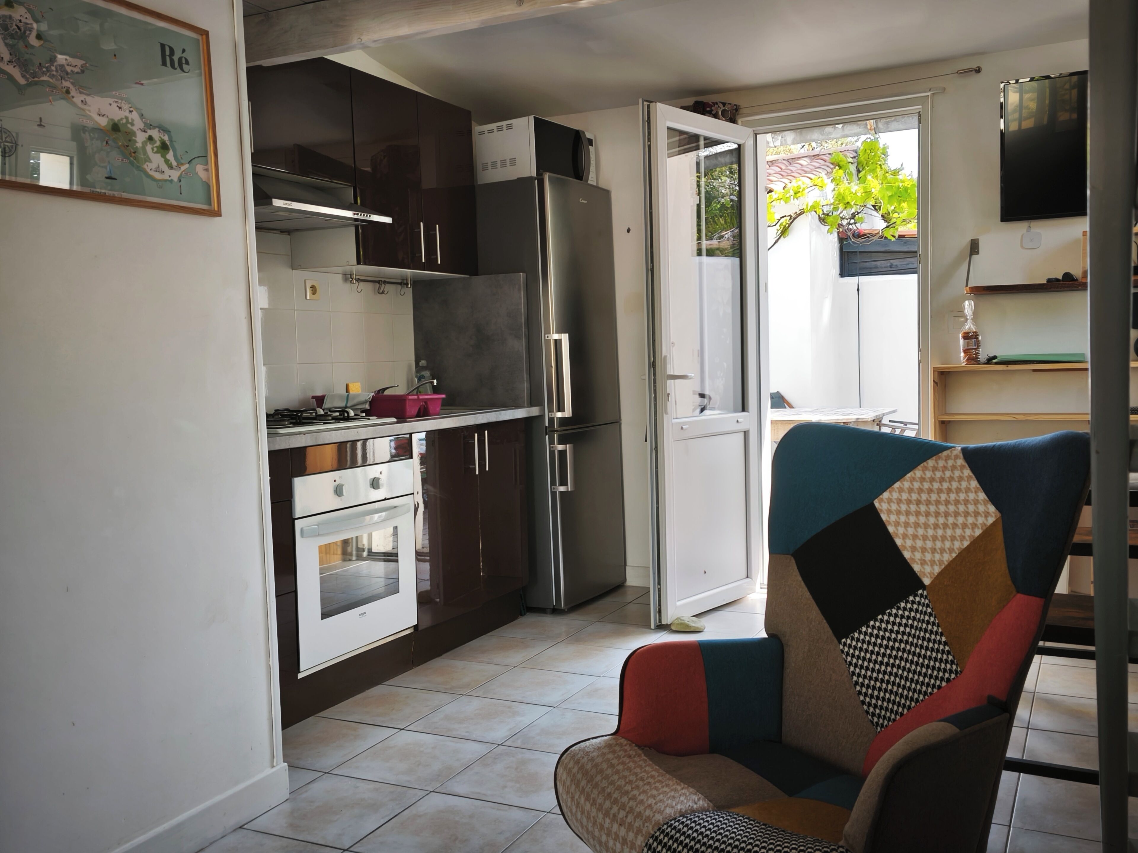 A compact kitchen with a refrigerator, oven, and a dining area with a colorful chair.