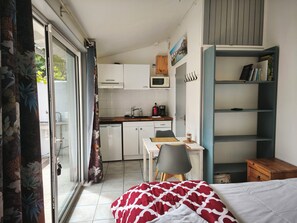 Una habitación compacta con cama, escritorio, silla, kitchenette pequeña y estantería.