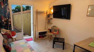 A room with a bed, a table, a chair, a TV, and a sliding door leading to an outdoor area.