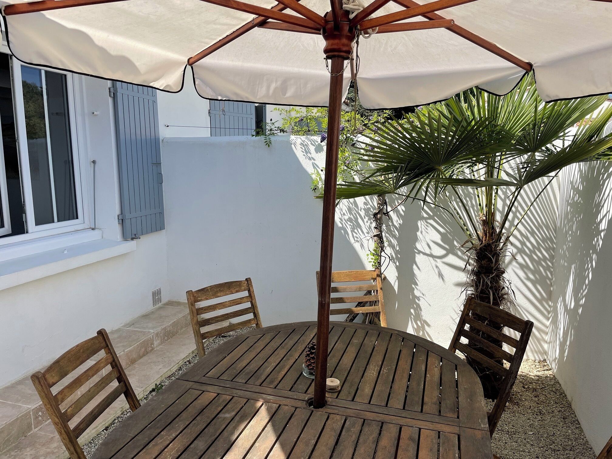 A round wooden table with four chairs, an umbrella, and a potted plant.