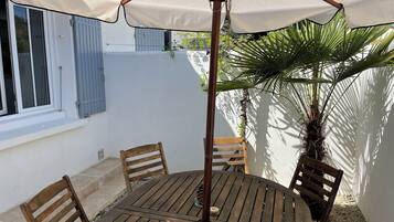 A round wooden table with four chairs, an umbrella, and a potted plant.