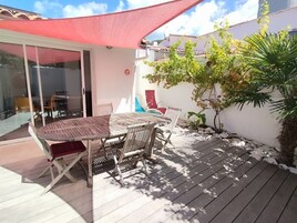 Une terrasse avec une table et des chaises, un parasol rouge et un petit arbre.