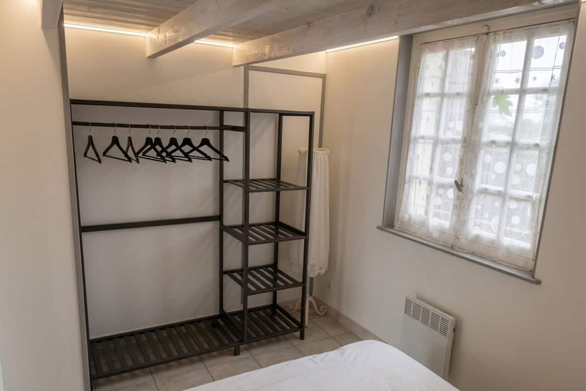 Une chambre à coucher avec un lit, une armoire avec des étagères, une fenêtre avec des rideaux et un radiateur.