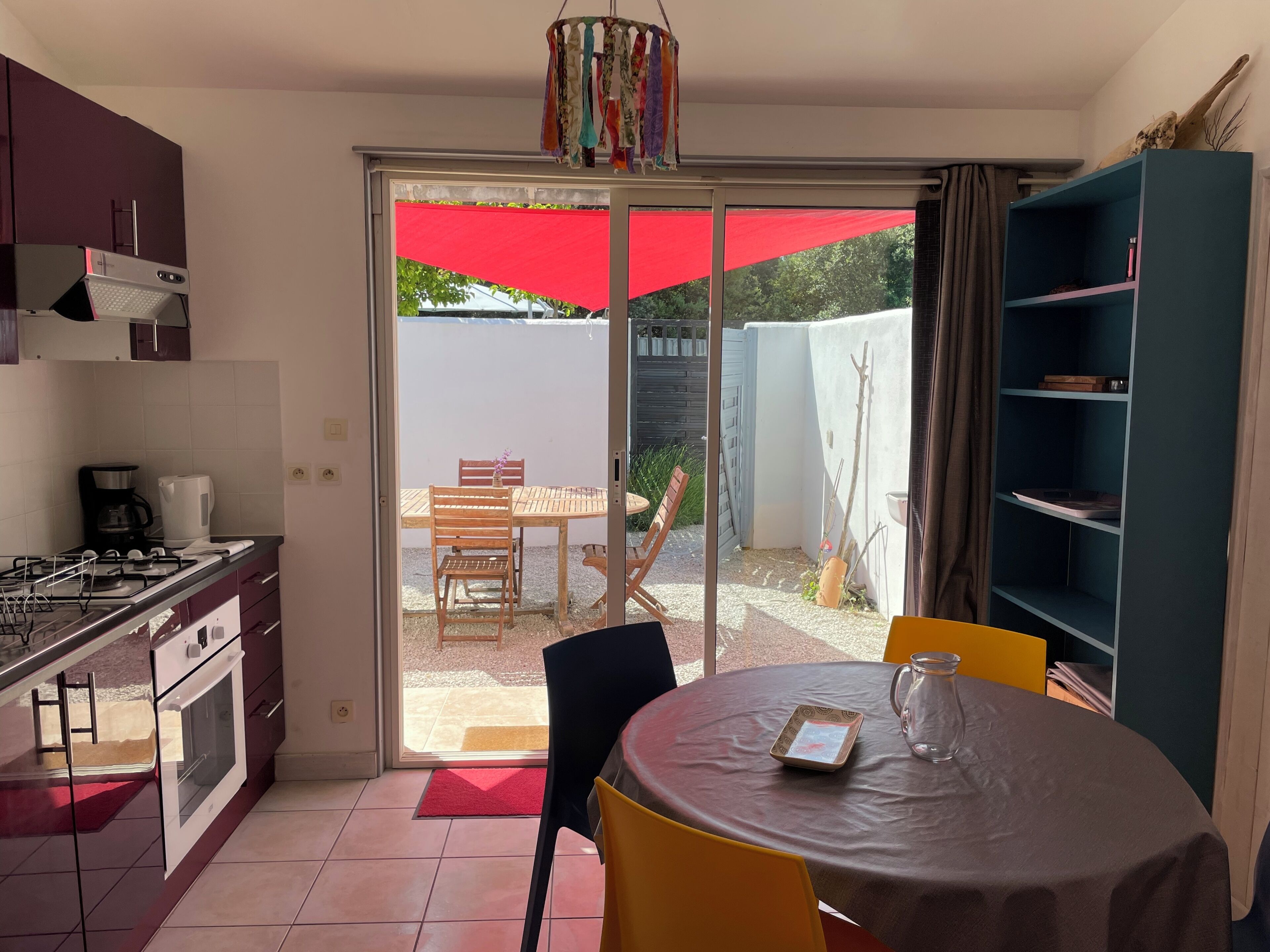 Una cocina compacta con estufa a gas, horno y cafetera, un comedor con mesa y sillas, y una puerta corrediza de vidrio que da a un patio exterior.