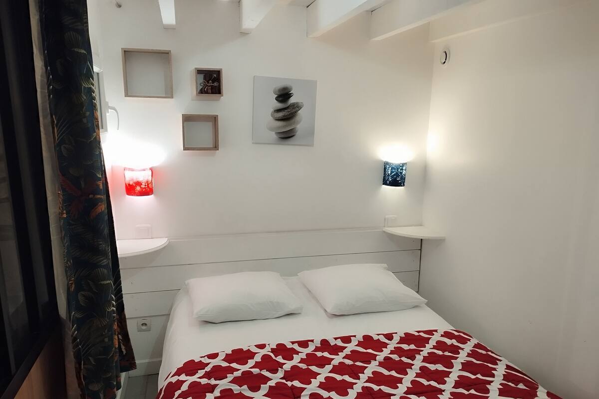 Une chambre à coucher comprenant un lit, deux tables de chevet, une étagère fixée au mur, une œuvre d’art encadrée et un luminaire fixé au mur.