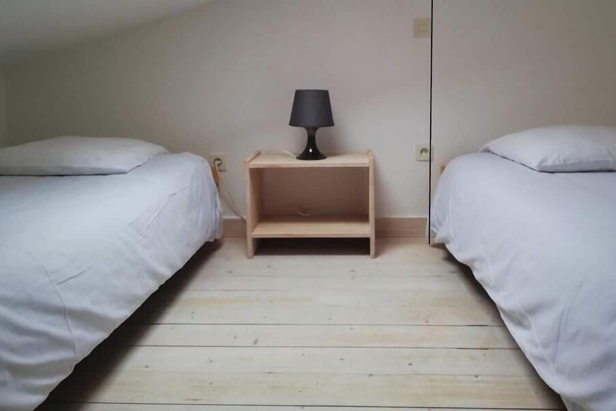 Une chambre avec deux lits, une table de chevet avec une lampe et un plancher en bois.