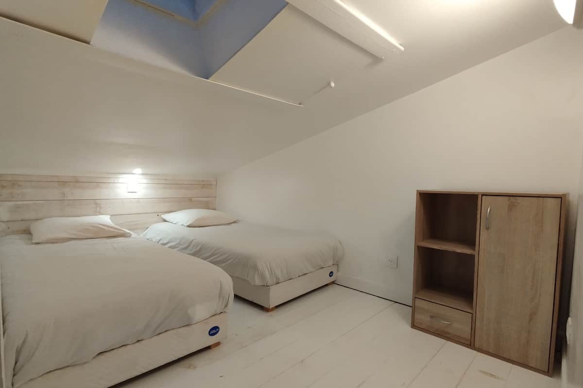 Une chambre avec deux lits, une armoire en bois et un plafond en pente doté d’un puits de lumière.