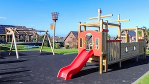 A playground with a red slide, swings, and a climbing structure. - Warleggan (Redruth)