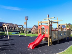 Un parque infantil con un tobogán rojo, columpios y una estructura para escalar.