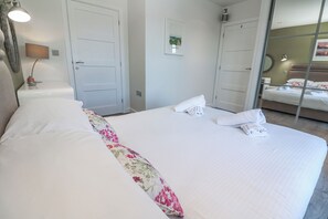 Ein Hotelzimmer mit einem großen Bett, einem Nachttisch mit Lampe, einem Spiegel und einer Tür.