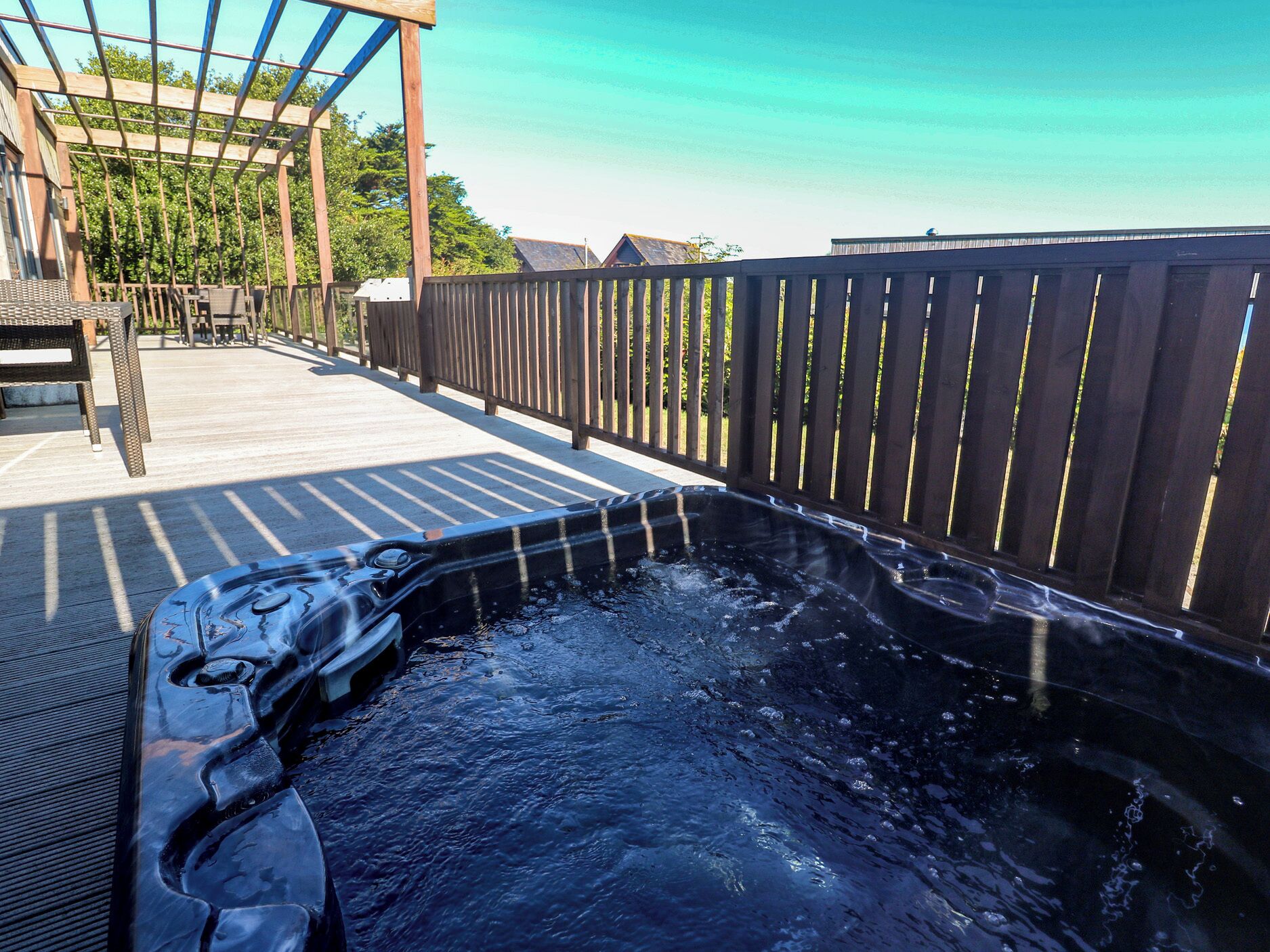 A hot tub on a wooden deck with a pergola and outdoor furniture.