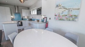 A modern kitchen with white cabinets, a central island, and a dining area with a white table and chairs. - Warleggan (Redruth)