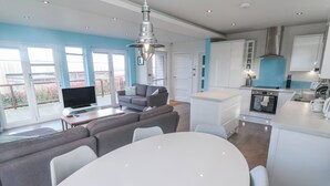 A modern kitchen with white cabinets, a built-in oven, and a dining area with a white table and chairs. - Warleggan (Redruth)