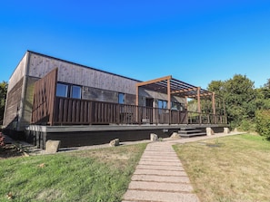 Un edificio moderno con facciata in legno, una zona esterna coperta e un vialetto in pietra che conduce all'ingresso.