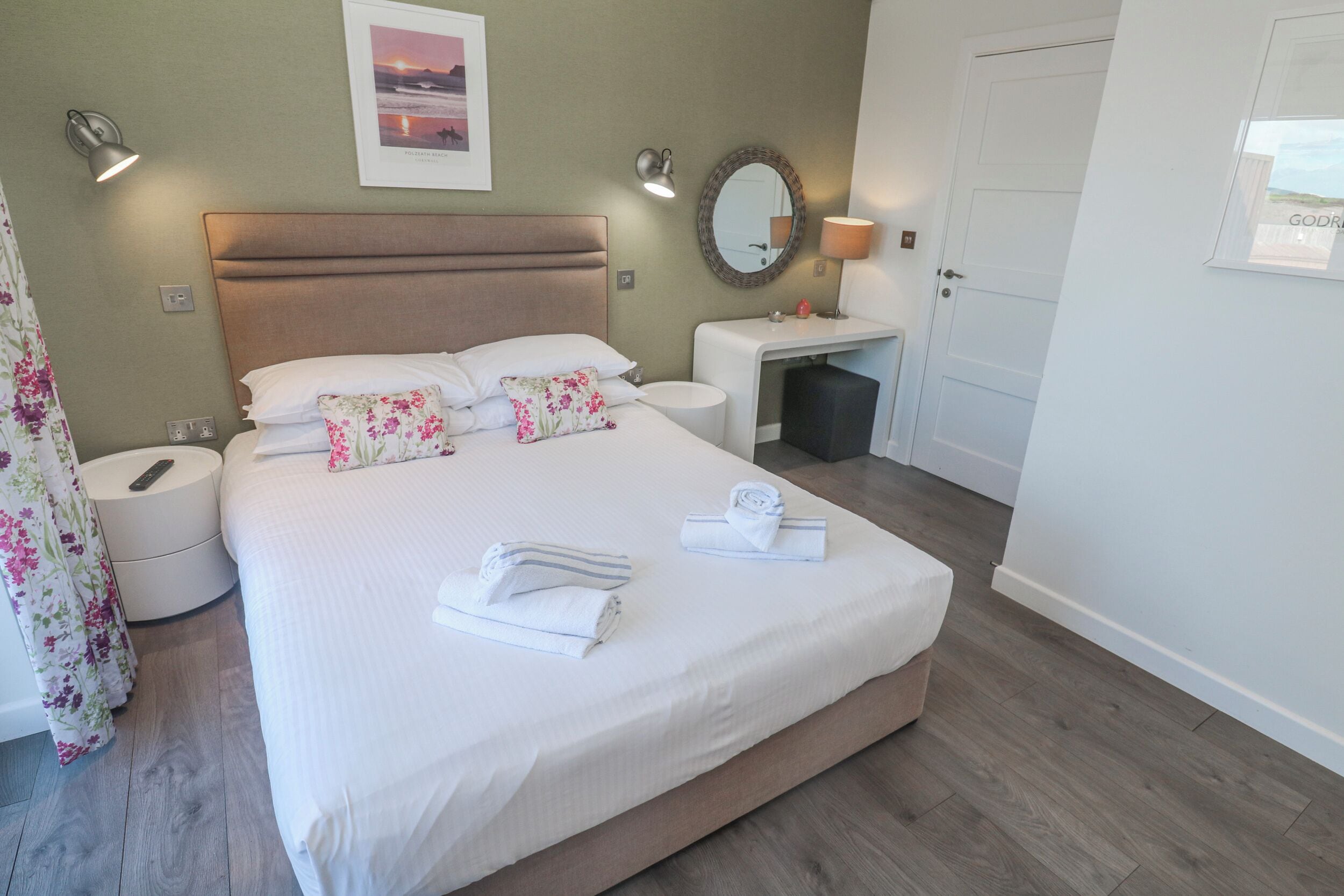 A neatly arranged hotel room with a bed, bedside tables, a mirror, and a framed picture on the wall.