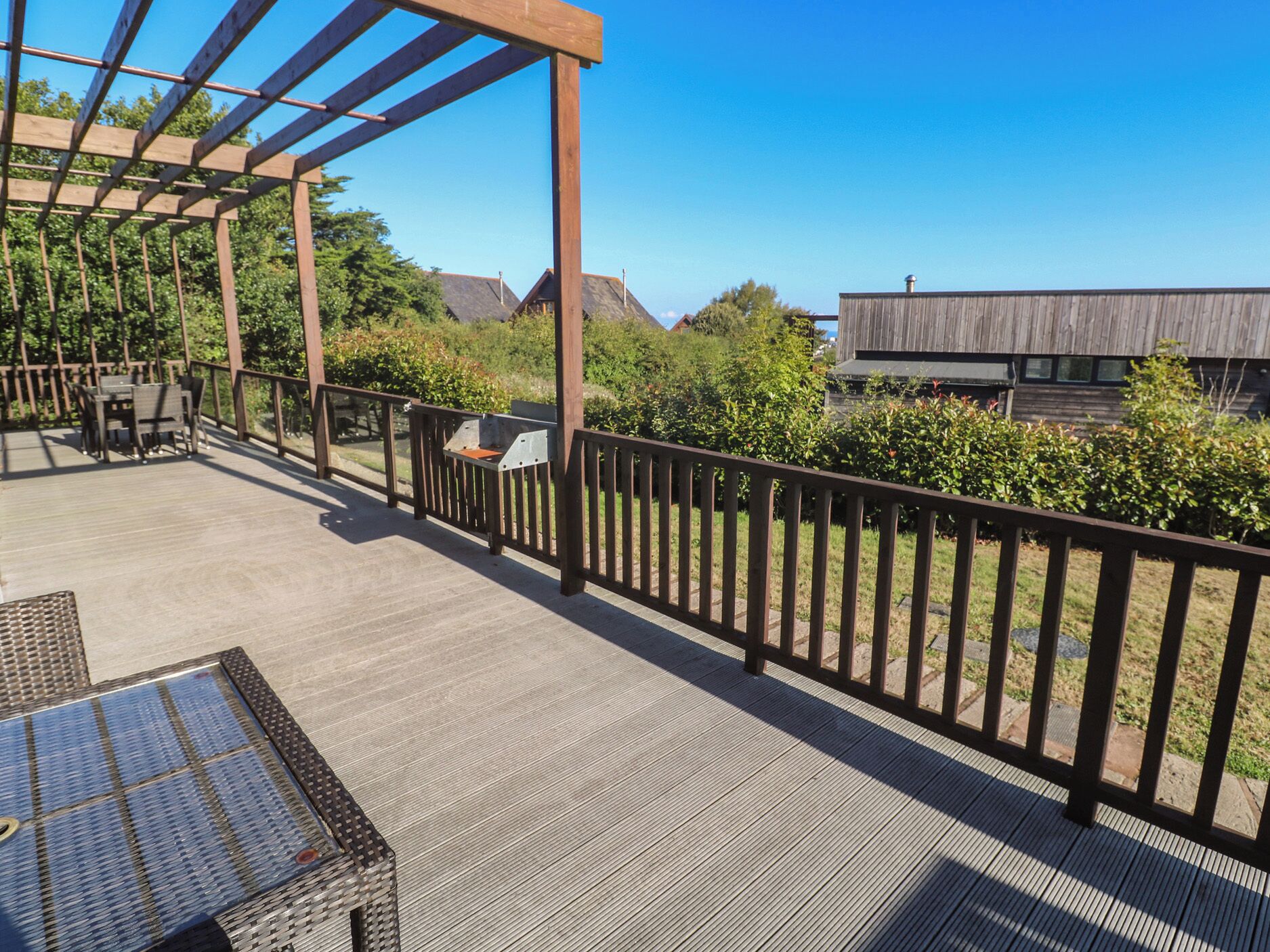 Una terraza de madera con pérgola, mobiliario exterior y vistas a edificios al fondo.