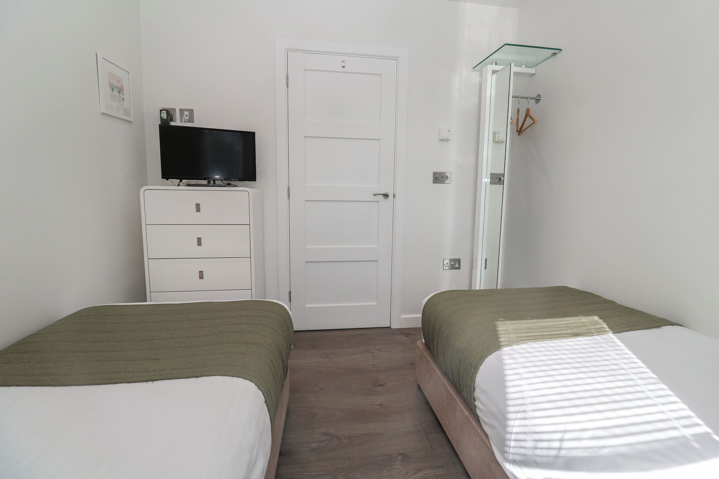 Un dormitorio con dos camas, un televisor sobre una cómoda, una puerta y una zona de ducha.