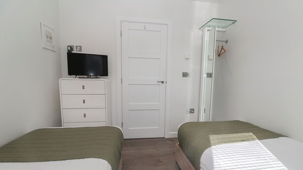 A bedroom with two beds, a TV on a dresser, a door, and a shower area. - Warleggan (Redruth)