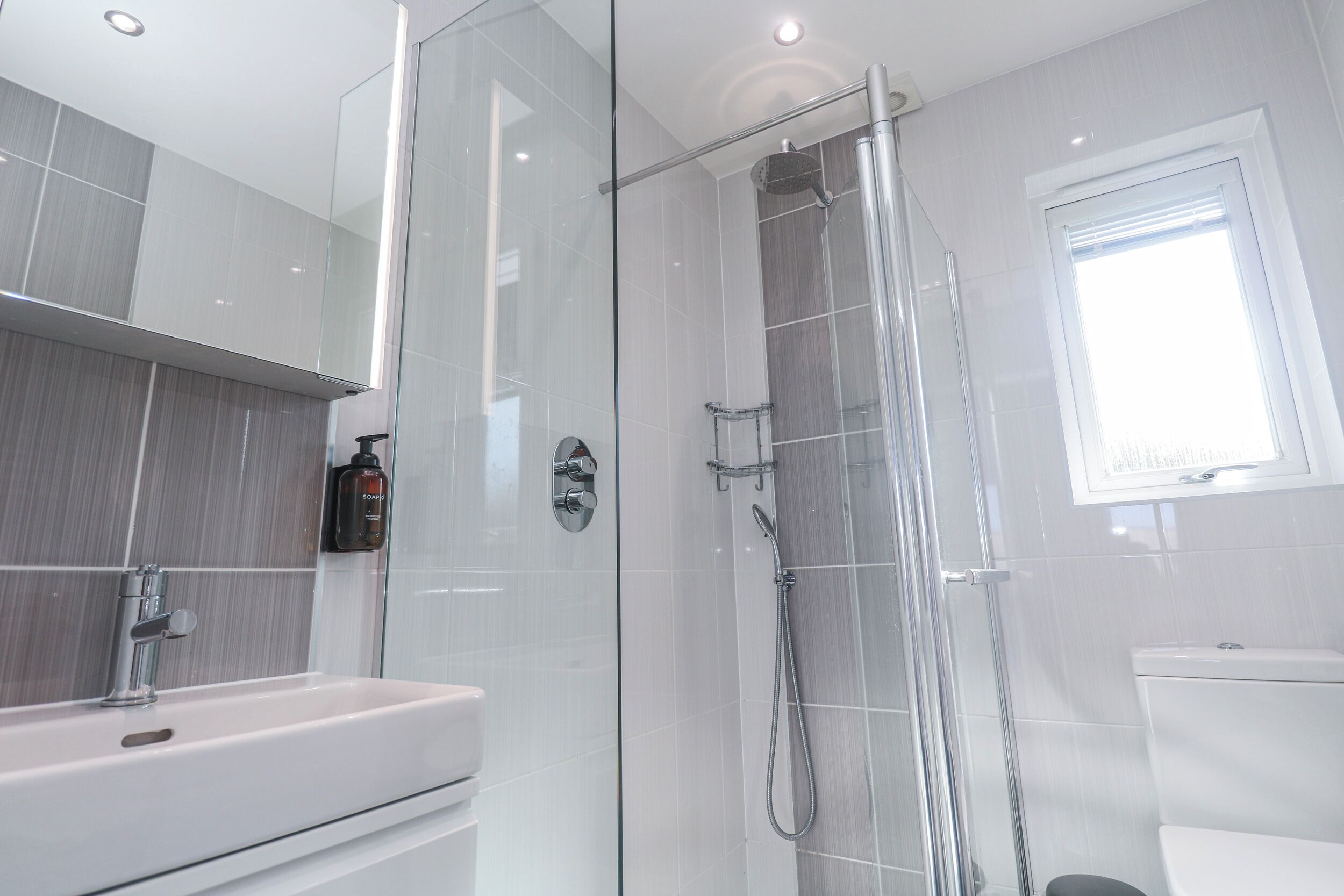 A modern bathroom with a glass-enclosed shower, a white sink, and a toilet.