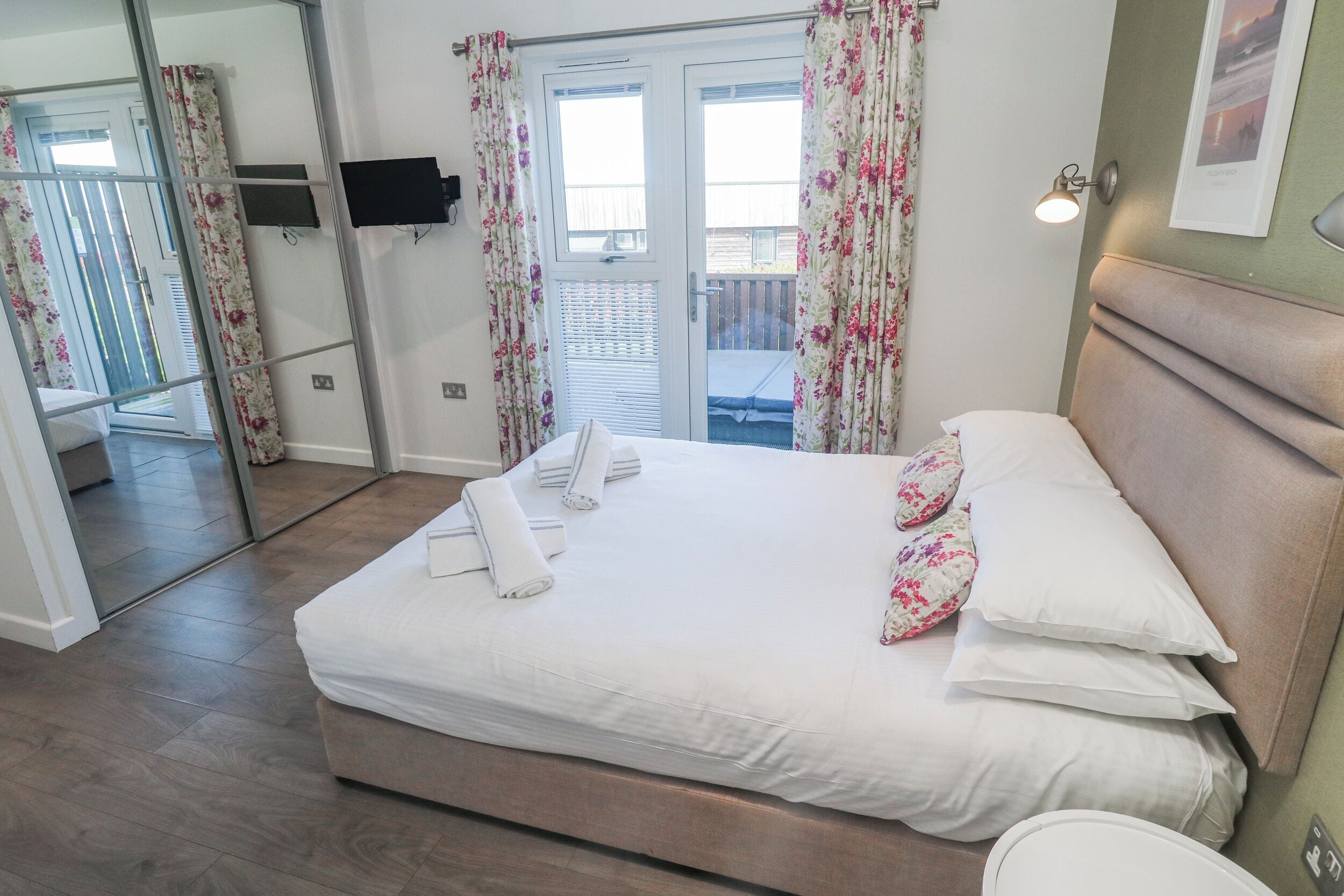 A bedroom with a bed, a flat-screen TV, a balcony, and a door with curtains.