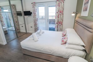 A bedroom with a bed, a flat-screen TV, a balcony, and a door with curtains. - Warleggan (Redruth)