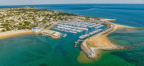 Oversigtsbillede af en kystmarina med mange både i havnen, en sandstrand og et boligområde i baggrunden.