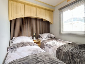 A bedroom with two beds, a wooden headboard, a bedside table with a lamp, and a window with blinds. - The Granada at Argraig (Holyhead)