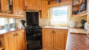 Una cocina con armarios de madera, estufa negra, ventana y encimera con cafetera.