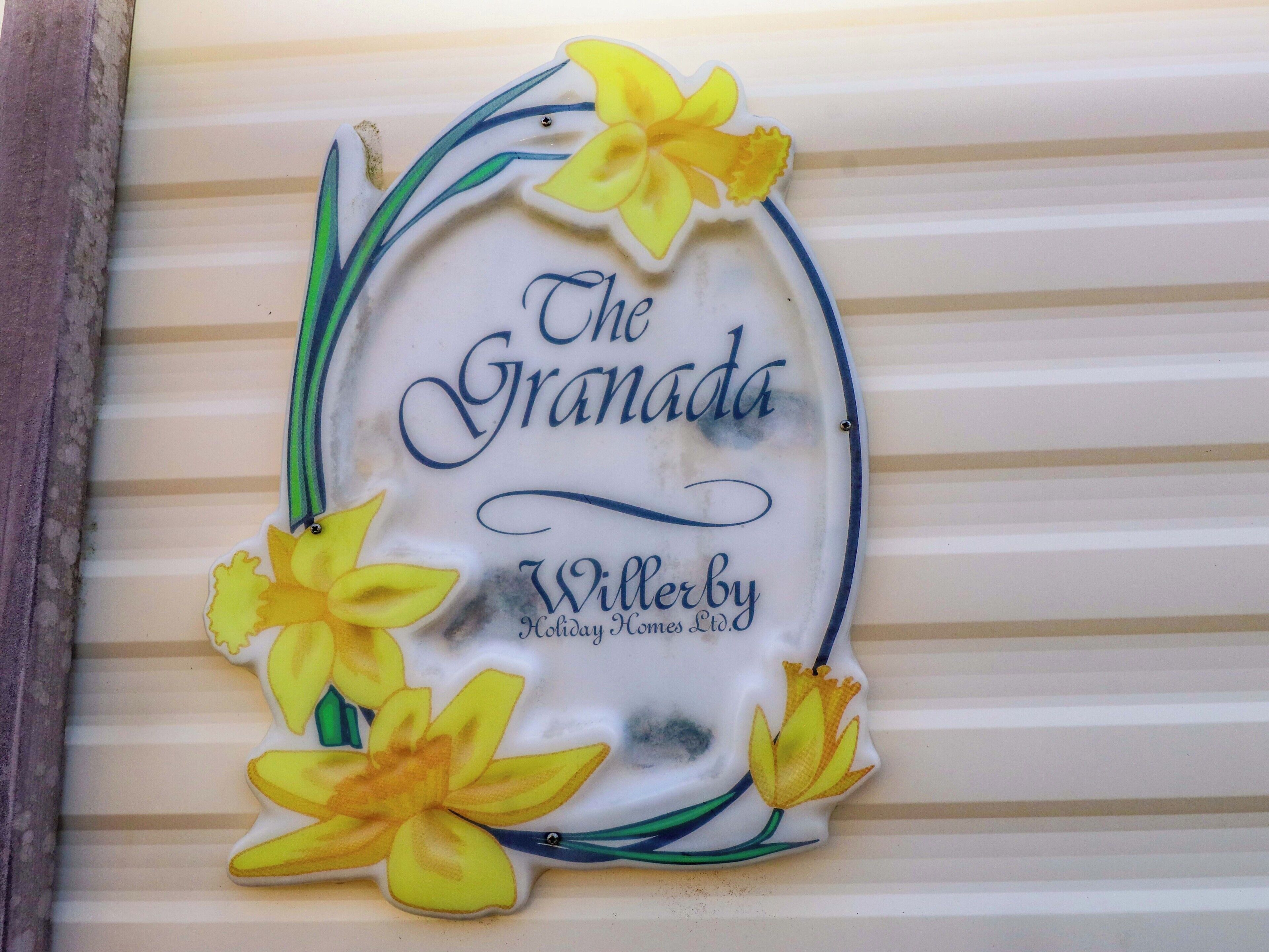 A decorative sign with the text 'The Granada' and 'Willerby Holiday Homes Ltd.' surrounded by yellow flowers.
