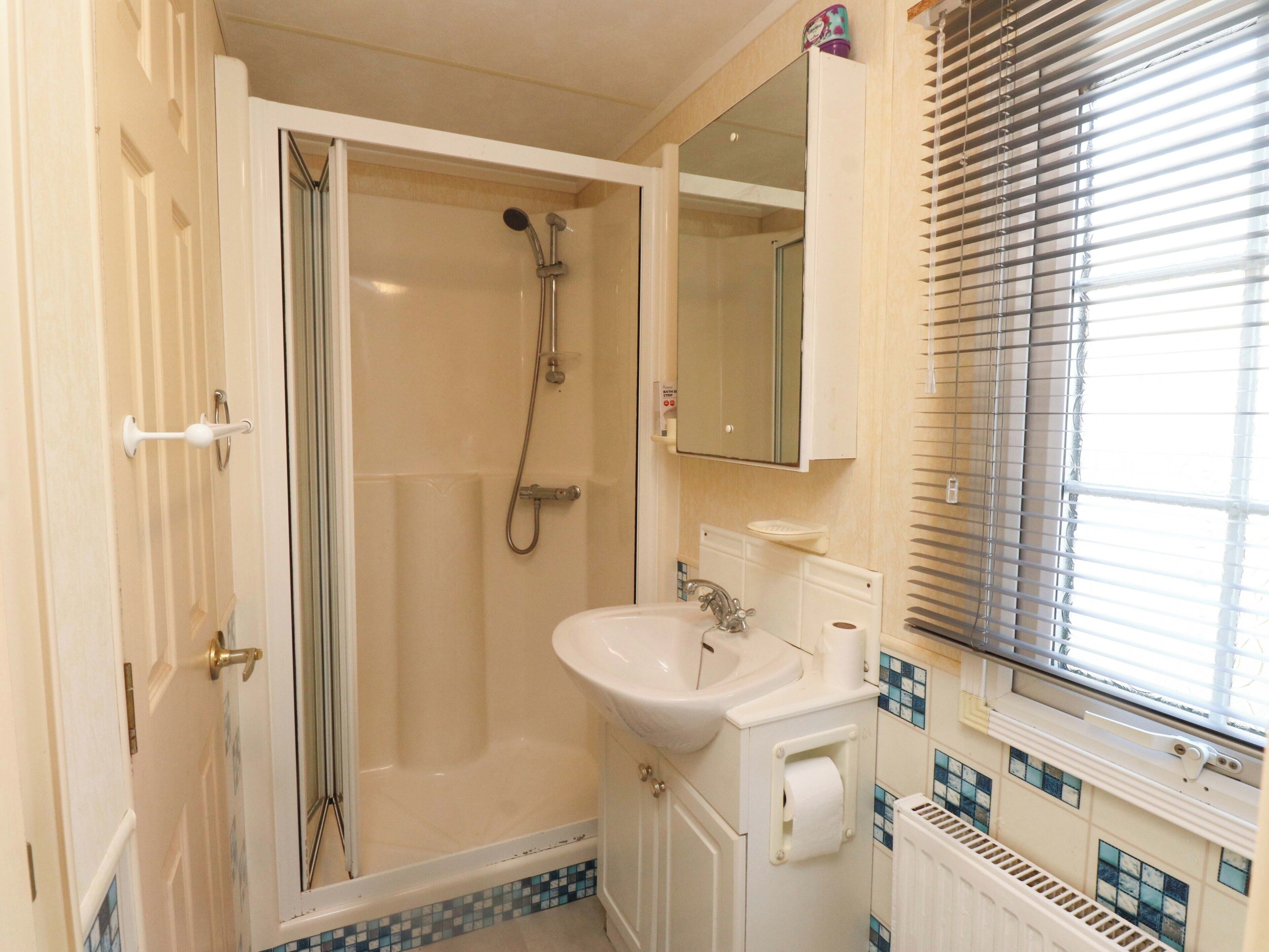 A bathroom with a shower, sink, toilet, and a window with blinds.