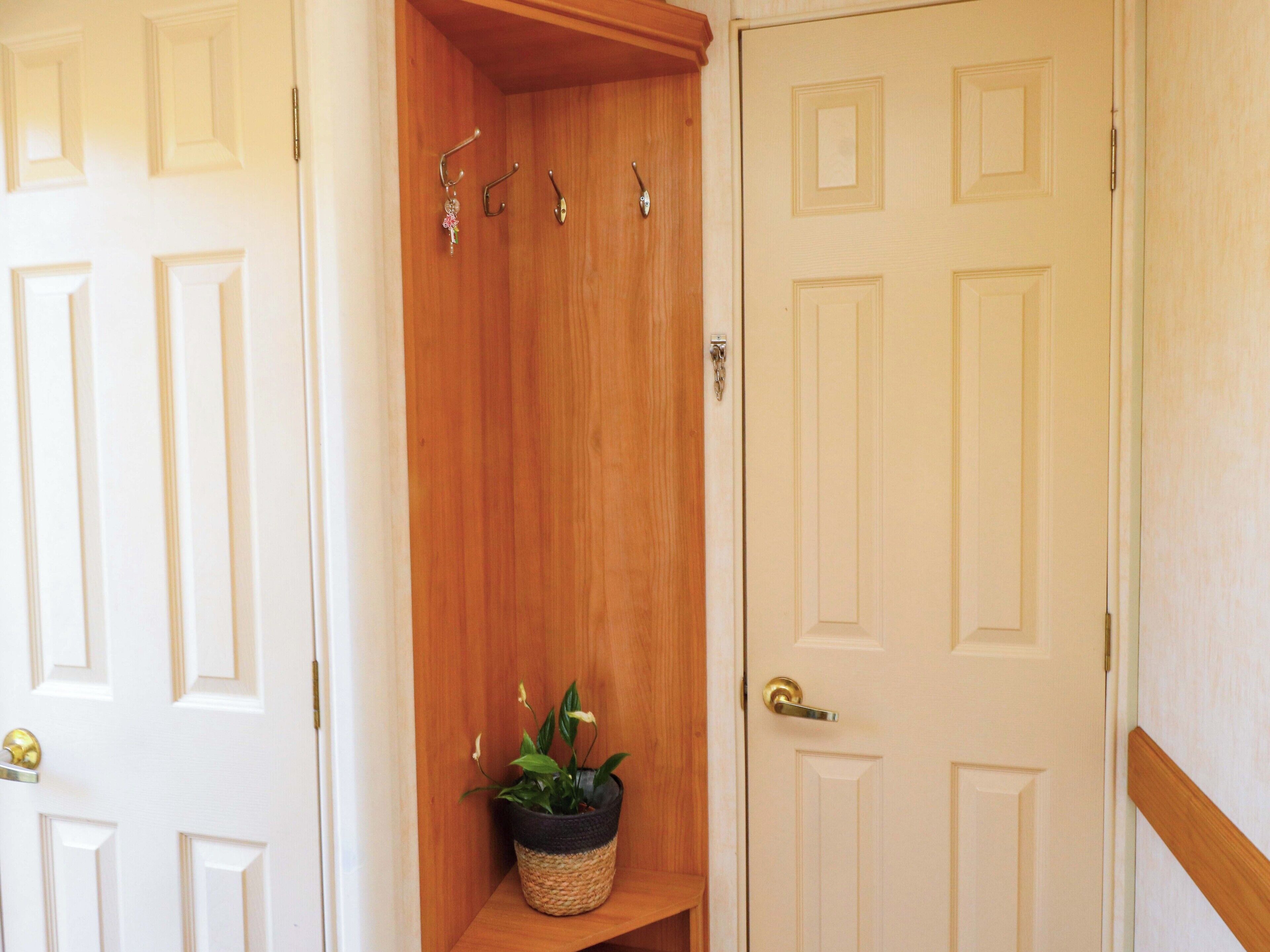 Un pasillo con un estante de madera, una planta en maceta y una puerta con picaporte de latón.