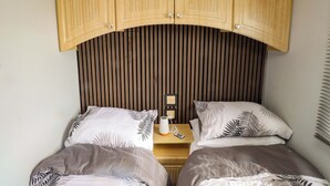 Un dormitorio con dos camas, cabeceros de madera, una mesita de noche con lámpara y un enchufe.