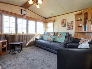 A cozy living room with a sofa, a small table, a radiator, and a window with blinds. - The Granada at Argraig (Holyhead)