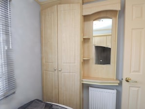 A room with a wooden wardrobe, a mirror, and a radiator. - The Granada at Argraig (Holyhead)