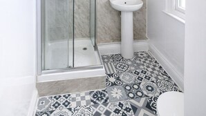 A modern bathroom with a glass shower enclosure, a pedestal sink, and patterned floor tiles. - Hammersmith Stayz (London)