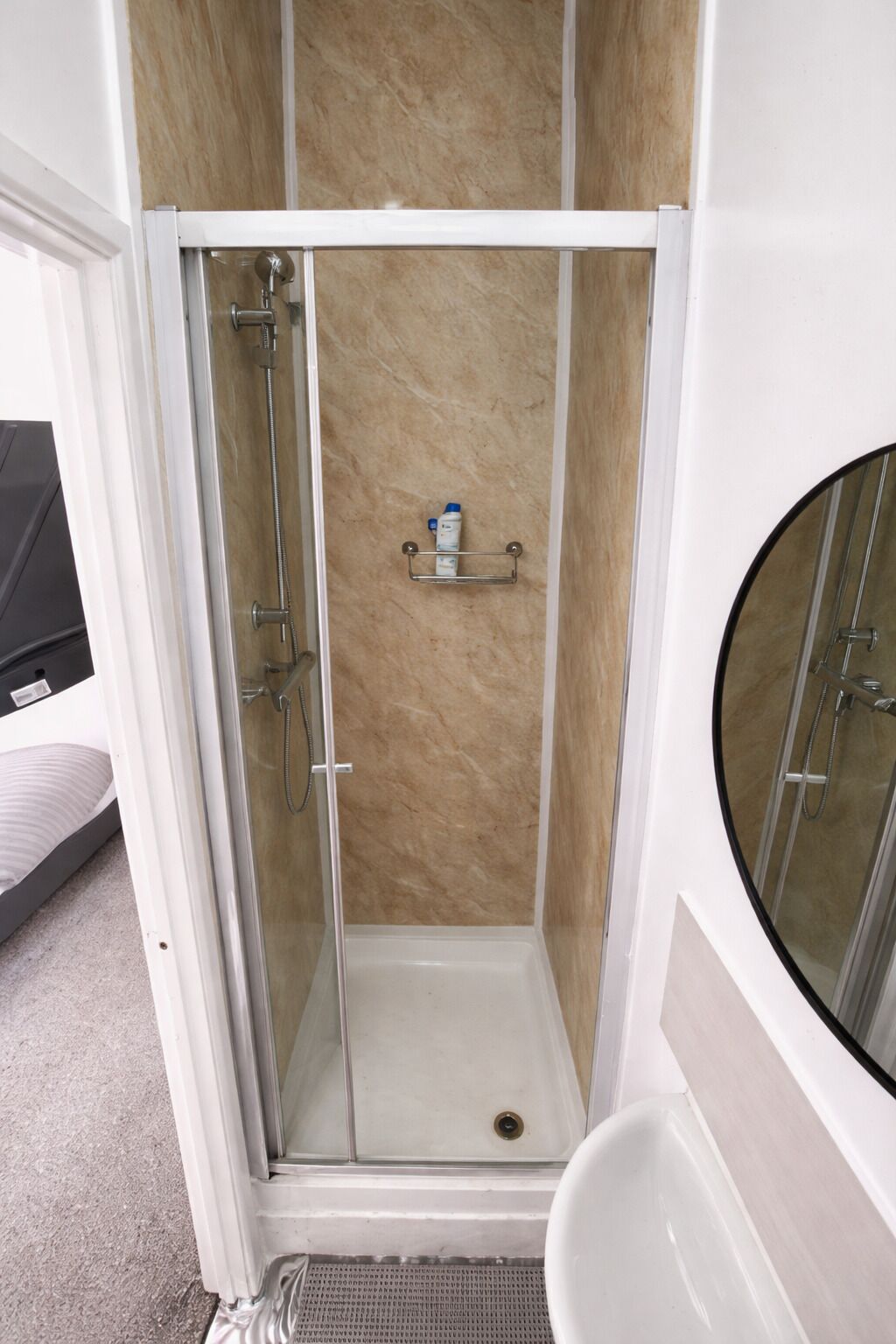 Eine bodenebene Dusche mit beige fliesigen Wänden, einer Glastür und einer kleinen Ablage für Toilettenartikel.