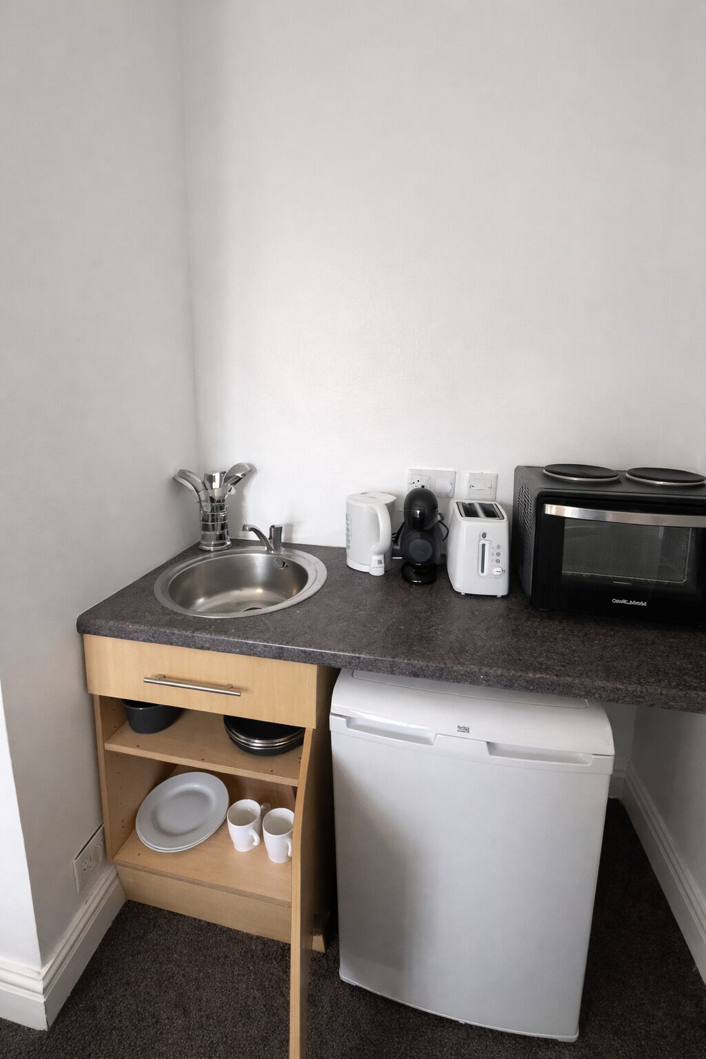 A compact kitchenette with a sink, toaster, coffee maker, and a small refrigerator.