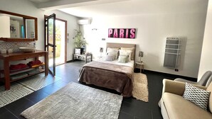 Un dormitorio con cama, mesitas de noche, un espejo, aire acondicionado montado en la pared, un radiador y un letrero grande que dice 'PARIS'.
