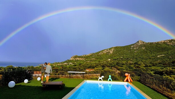 Piscina con vista a una montaña y al mar, rodeada por una zona vallada con detalles decorativos.