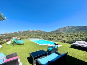 Une piscine avec vue sur les montagnes, des meubles d’extérieur et un ciel dégagé.