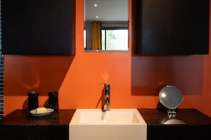 Une salle de bain avec un lavabo blanc, un miroir et deux vases noirs posés sur le comptoir.