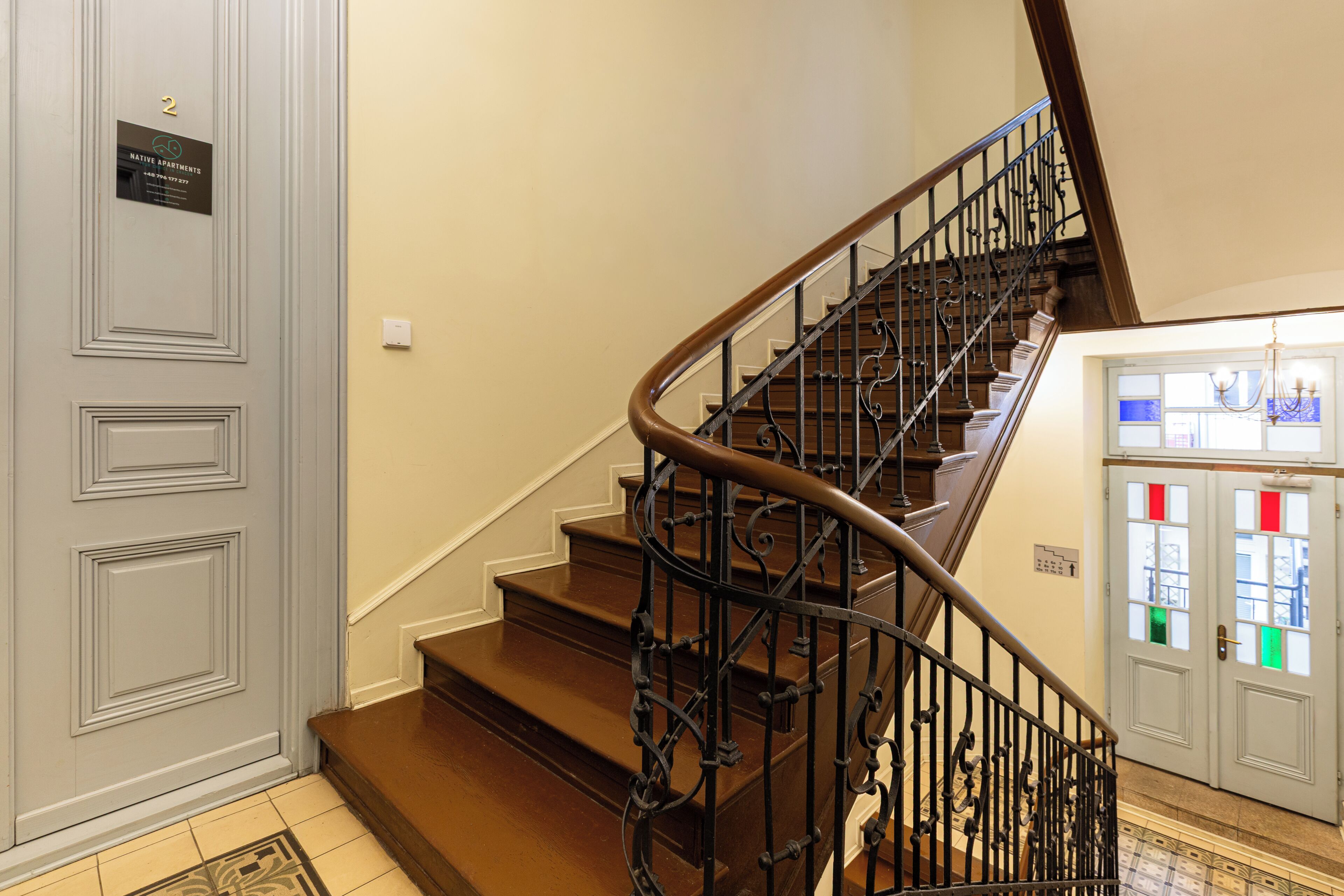 A staircase with a wooden handrail and black metal balusters, leading to a landing with a door marked '2'.