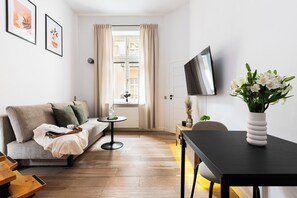 A modern living room with a sofa, a coffee table, a TV, and a vase with flowers. - Native Apartments Brzozowa 8 (Kraków)