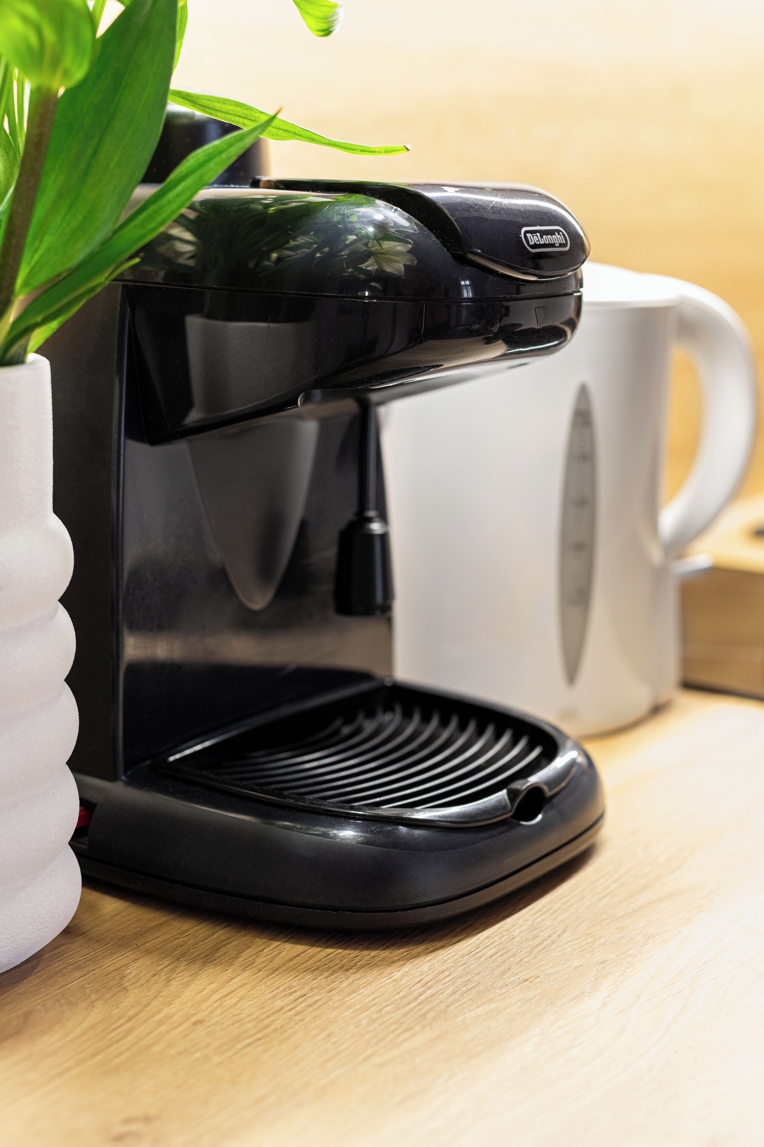 A black coffee maker with a white mug and a white container on a wooden surface.