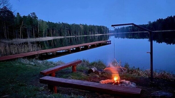 A lakeside setting with a dock, a fire pit, and a picnic table.