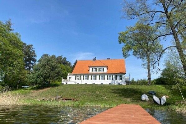 A house with a red roof, a wooden dock, and a pond.