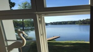 A view through a window with a wooden swan decoration, a lake, and a dock.
